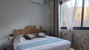 Ein Schlafzimmer mit einem Holz-Kopfteil, einem Bett mit blauer Bettdecke, einer Steinwand und einem Fenster mit Vorhängen.