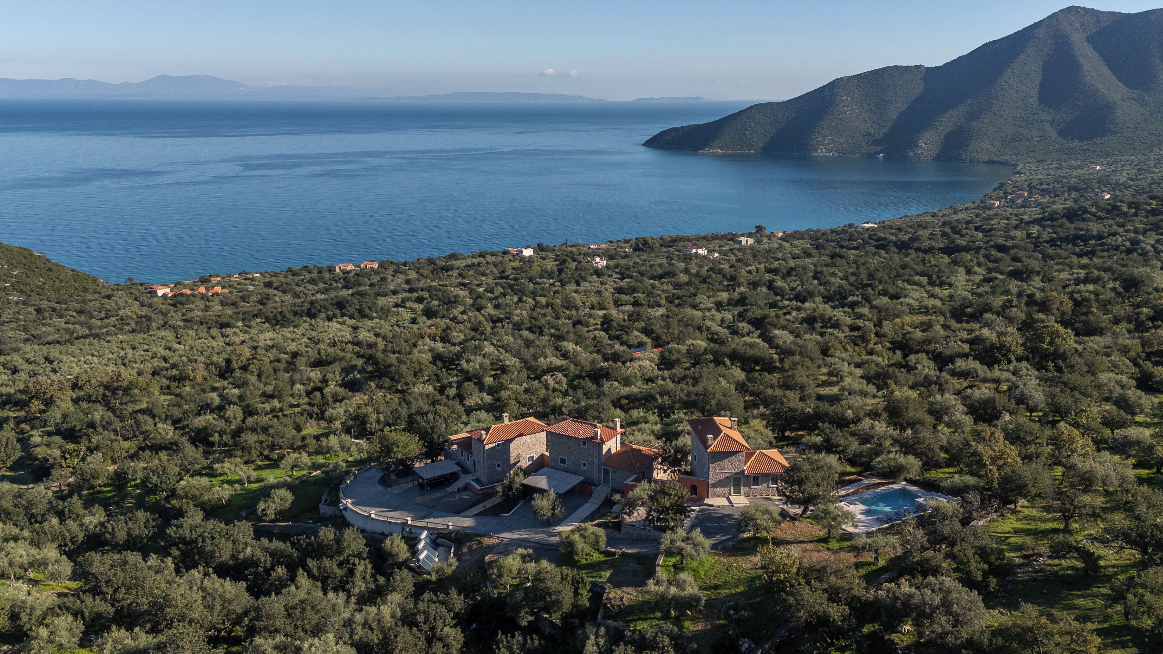 A coastal property with a swimming pool, surrounded by dense greenery and overlooking a large body of water.