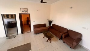 A living room with a brown sofa set, a glass coffee table, and a ceiling fan. - 3-bedroom farmhouse in outskirts of Mohali with AC comfort (Kurali)