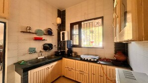 A compact kitchen with wooden cabinets, a black countertop, and a window with bars. - 3-bedroom farmhouse in outskirts of Mohali with AC comfort (Kurali)