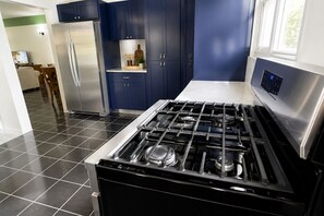 A modern kitchen with a stainless steel stove, blue cabinets, and a refrigerator.