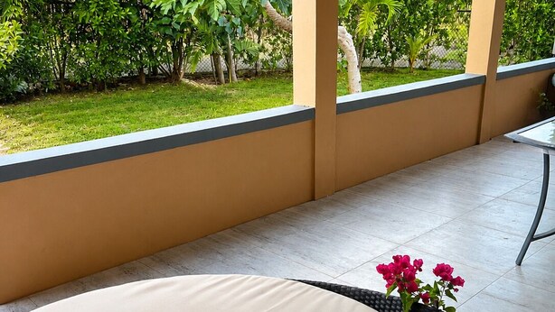 A covered outdoor seating area with a cushioned bench, a small table with a vase of flowers, and a view of lush greenery. - Clifton House -Falmouth, Antigua - 3 Bed 2 Bath (St. Paul's)