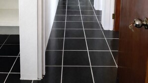 A hallway with black and white tiled flooring, a white door on the right, and a grey chair in the background. - Clifton House -Falmouth, Antigua - 3 Bed 2 Bath (St. Paul's)