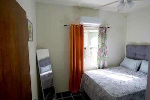 Un dormitorio con cama, ventana con cortinas, equipo de aire acondicionado y ventilador de techo.