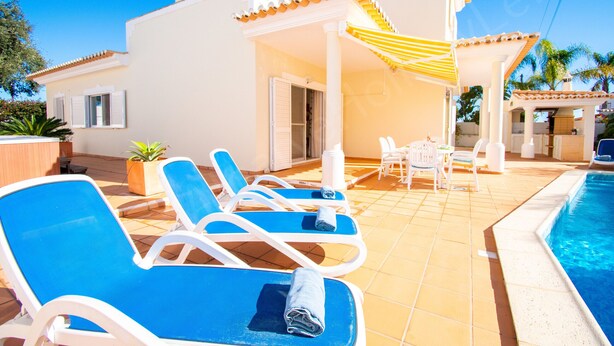 A poolside area with blue lounge chairs, a covered seating area, and a swimming pool. - Casa Destino | professionally cleaned | 3-bedroom villa | pool (Carvoeiro)