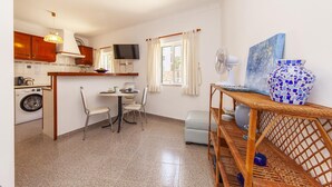 A compact kitchen with a washing machine, a dining area with chairs, a TV, and a fan. - A75 - Casa da Ponte 1 Bed Flat in Lagos (Lagos)
