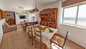 A dining area with a table set for four, wooden chairs, a lace tablecloth, and a view of the sea through a large window. - B83 - Calheta Terrace View Apartment (Lagos)