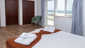 A hotel room with two wooden doors, a window with a view of the sea, a bed with white linens, and a green chair. - B83 - Calheta Terrace View Apartment (Lagos)