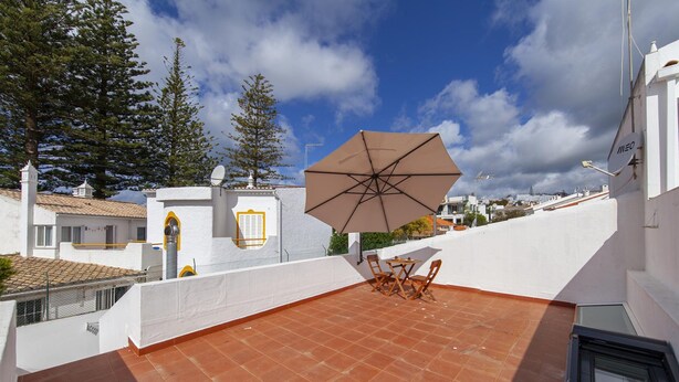 A rooftop terrace with a table and chairs, a large umbrella, and a view of the surrounding buildings and trees. - A20 - Beco Luz Studio (Lagos)