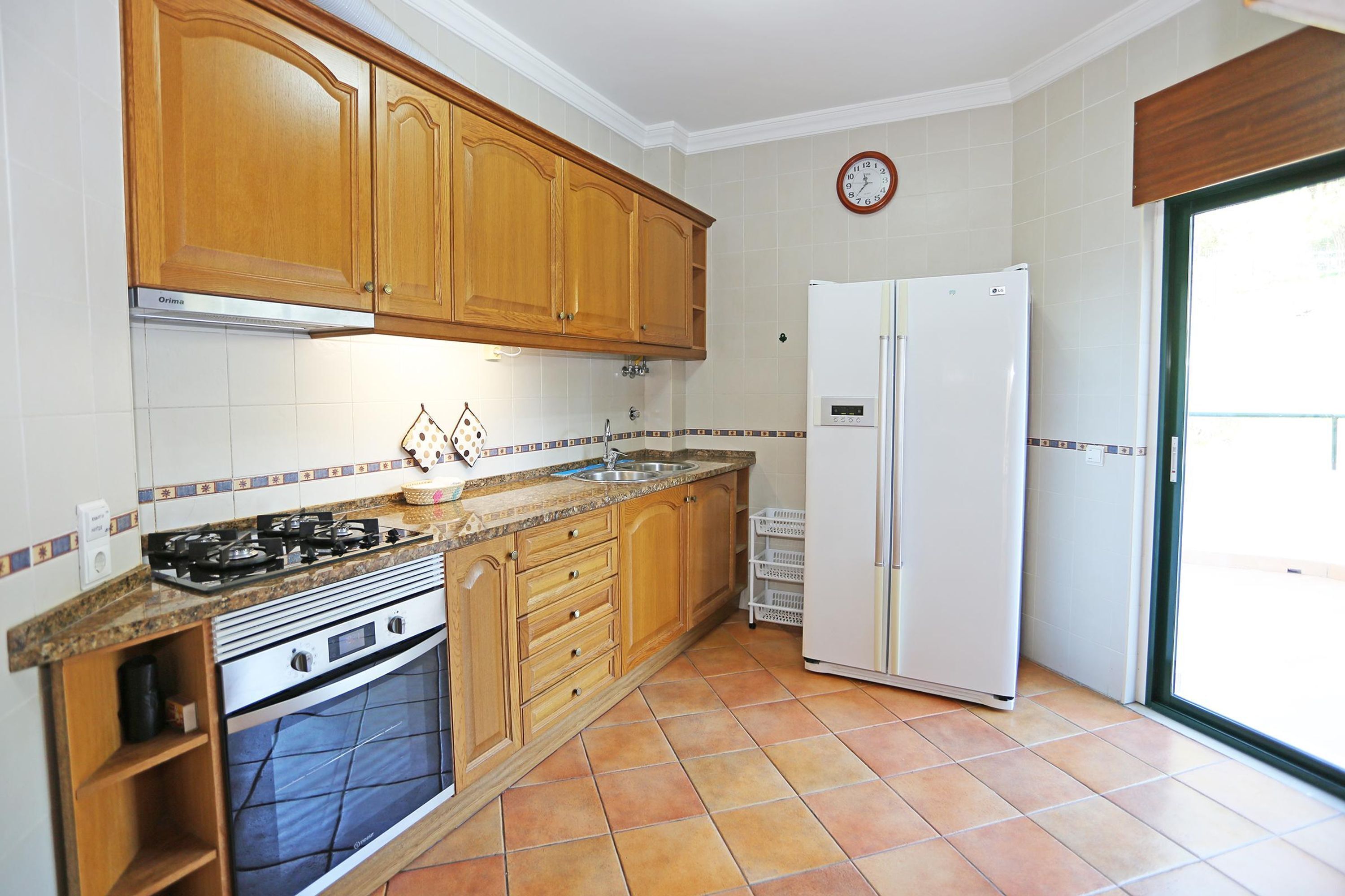A kitchen with wooden cabinets, a gas stove, an oven, a sink, and a refrigerator.
