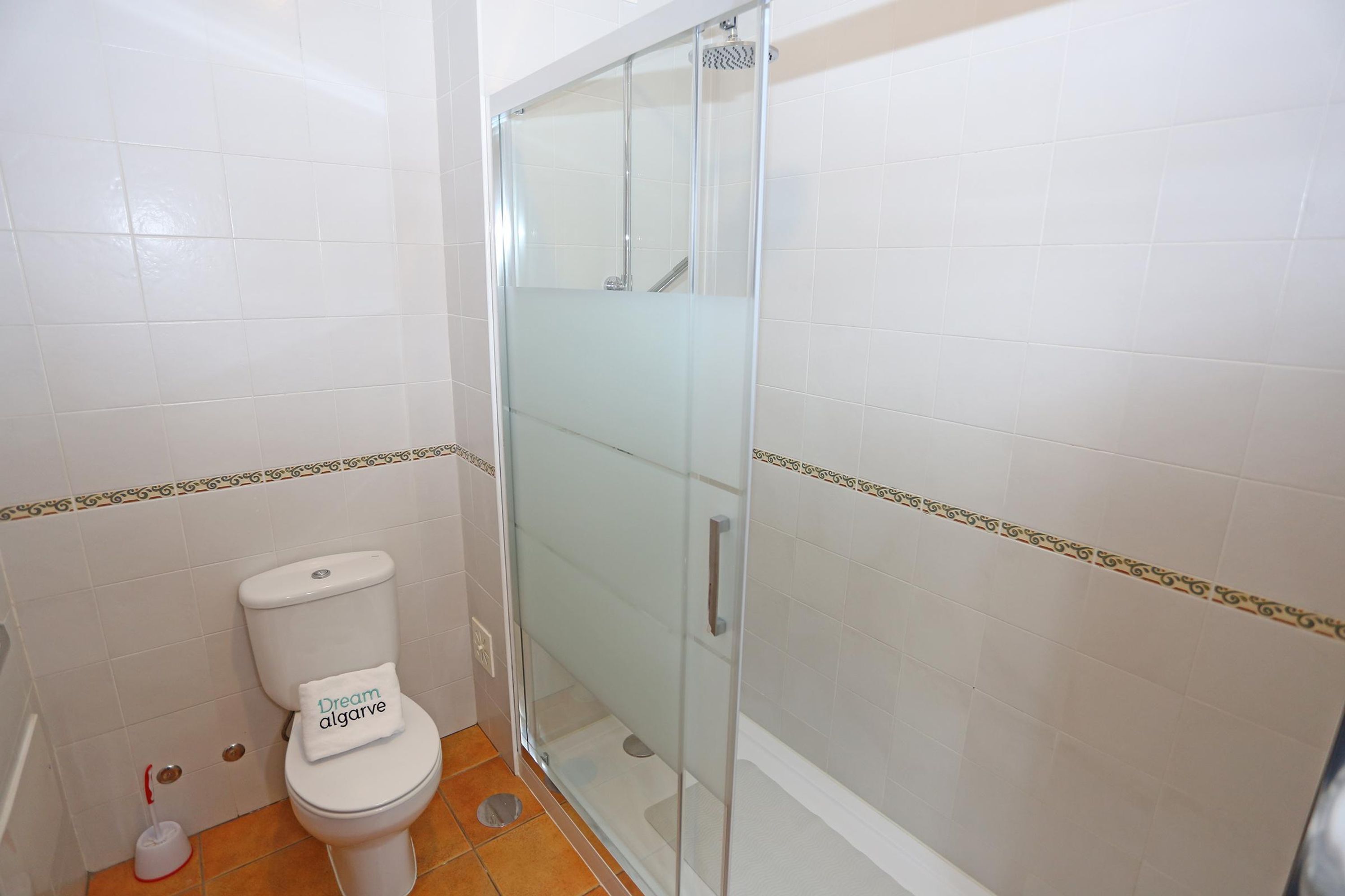 A bathroom with a toilet, a glass shower enclosure, and tiled walls.