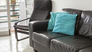 A dark leather sofa with two teal pillows, positioned near a window with a view of palm trees and a building outside. - B77 - Im on Avenida Apartment in Lagos (Lagos)