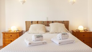 Siististi pedattu sänky, jossa on kaksi tyynyä, kaksi yöpöytää valaisimineen sekä pyyhkeet, joissa on teksti ”Dream Algarve”.
