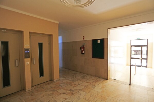 A hallway with two elevators, a fire extinguisher mounted on the wall, and a door leading to a bright room. - B98 - Rio a Vista Praia da Rocha Apartment (Portimão)