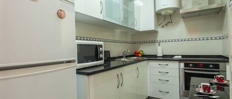 A modern kitchen with white cabinets, a microwave, a sink, and an oven.
