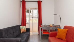 Ett kompakt vardagsrum med en svart soffa, en röd soffa, ett matbord med stolar och en röd gardin.