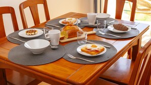 Una mesa de madera para comer con manteles individuales, platos de comida, tazas y cubiertos.