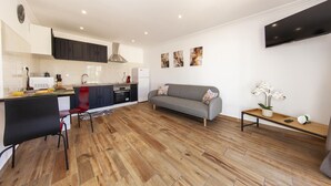 Una cucina moderna con mobili scuri, un'area pranzo con una sedia rossa, un divano grigio e una TV a parete.