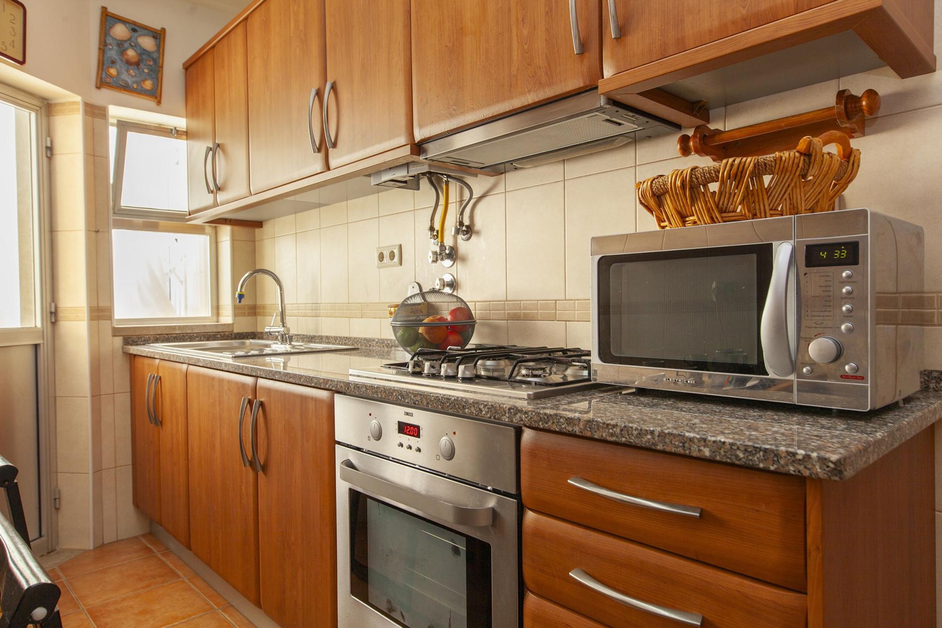 A kitchen with wooden cabinets, a gas stove, an oven, a microwave, and a sink.
