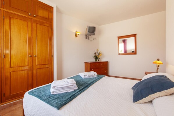 A hotel room with a bed, a wooden wardrobe, a desk with a lamp, and a television on the wall. - L 03 - Bedroom 3 Western Mos Guesthouse (Lagos)