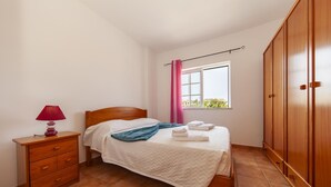 Ein Schlafzimmer mit einem hölzernen Bett, einem Nachttisch, einem Fenster mit Vorhängen und einem Kleiderschrank.