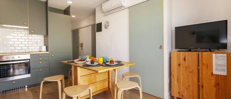 Cocina compacta con zona de comedor, sillas de madera, un televisor y un horno pequeño.