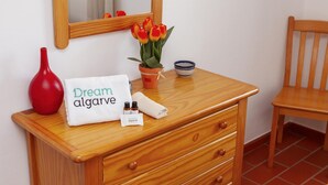 En trækommode med et spejl, en rød vase, en potteplante med gule tulipaner, et hvidt håndklæde med teksten 'Dream algarve', og en lille flaske.