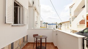 Un balcone con tavolo e sedie, una finestra con persiane e vista sugli edifici vicini.