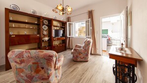 Un soggiorno con divano, poltrona, mensole in legno con piatti decorativi, un lampadario e vista panoramica attraverso una porta in vetro.