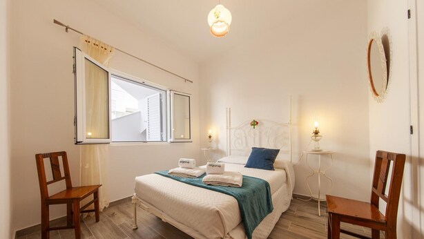 Una camera da letto con un letto, due sedie, una finestra e un comodino con una lampada.