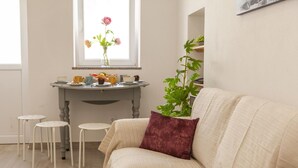 Ein gemütliches Wohnzimmer mit einem beigen Sofa, einem kleinen runden Tisch mit Blumen in einer Vase und einer Topfpflanze.