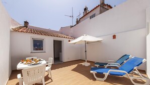 Eine Terrasse mit Esstisch, Sonnenschirm und Liegestühlen.