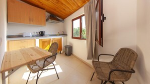 A compact kitchen with wooden cabinets, a dining table, wicker chairs, and a window with curtains. - H 06 - Samouqueira Studio in Montes de Praias (Aljezur)