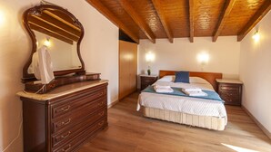 A bedroom with a wooden ceiling, a large mirror, a wooden dresser, a bed with a blue blanket, and two bedside tables with lamps. - H 06 - Samouqueira Studio in Montes de Praias (Aljezur)