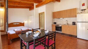 A compact room with a bed, a dining table with chairs, a kitchen area with wooden cabinets, and a water heater. - H 07 - Carreagem Beach Studio in Montes de Praias (Aljezur)