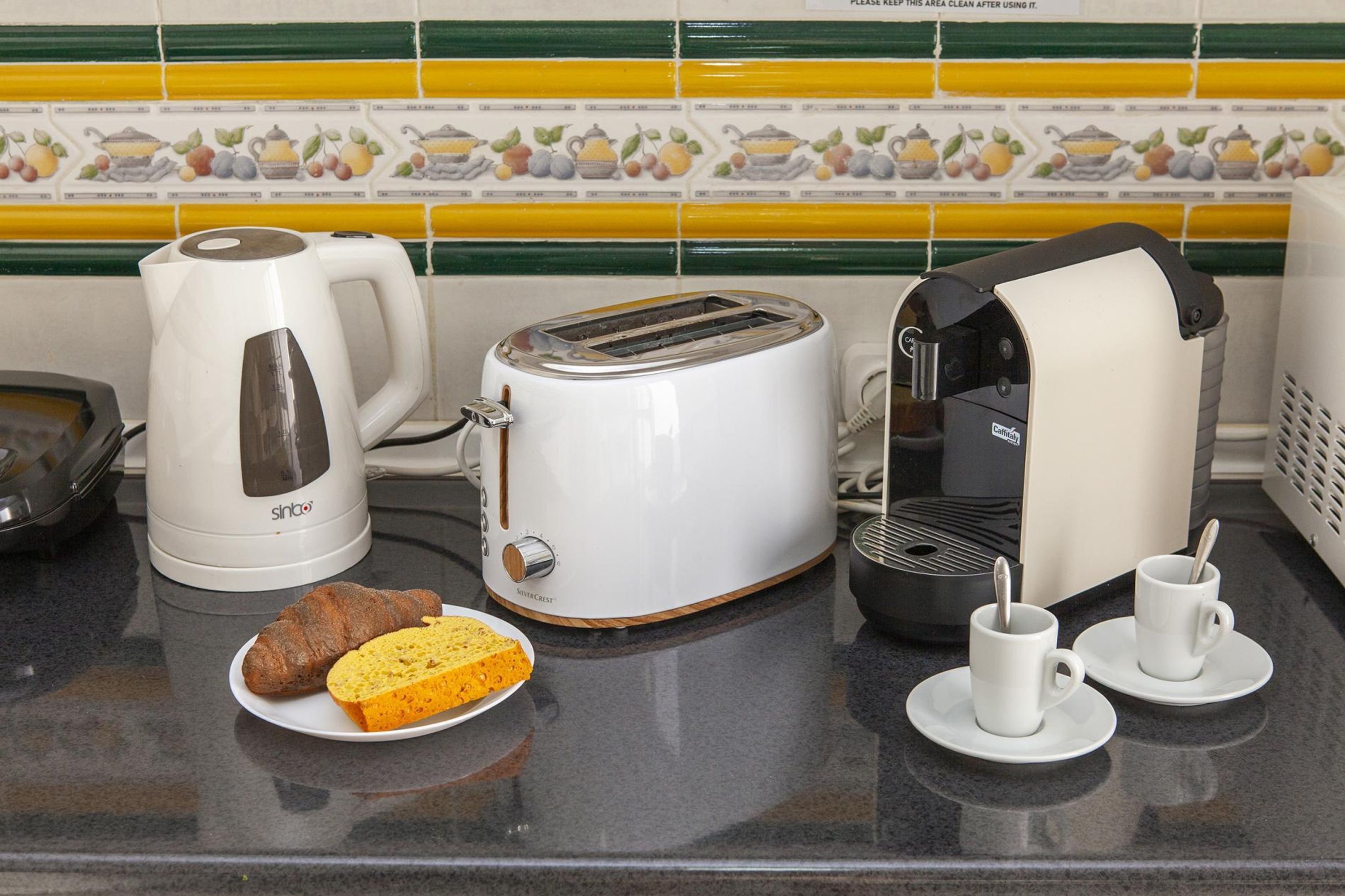 A kitchen counter with a coffee maker, toaster, and two cups on saucers.