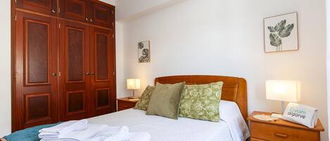 A hotel room with a large wooden wardrobe, a bed with a blue blanket, and two bedside tables with lamps.