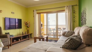 Ein Wohnzimmer mit Sofa, Fernseher und einer Schiebetür, die auf einen Balkon führt.