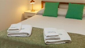 Una cama bien hecha con almohadas verdes, una lámpara de noche y toallas dobladas con un logotipo.