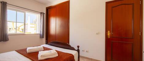 A hotel room with a bed, a wooden wardrobe, a door, and a window with curtains.