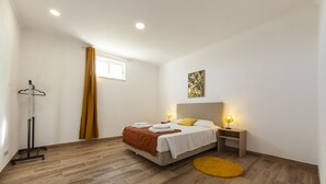 Une chambre à coucher comprenant un lit, des tables de chevet, un porte-manteau suspendu, une fenêtre avec des rideaux et une lampe sur pied.