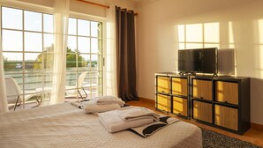A hotel room with a bed, a TV on a cabinet, a balcony with chairs, and a view of the outdoors. - B01 - Mar a Vista Rocha Apartment (Portimão)