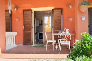 A patio with a table and chairs, a door leading to an interior space, and a small garden area. - Apartment 'Petit Verdot' with Shared Pool, Private Terrace and Shared Garden (Suvereto)
