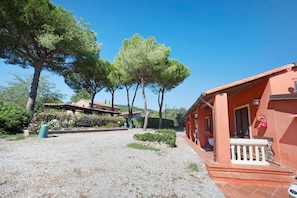 A building with a red facade, a gravel driveway, and surrounding trees. - Apartment 'Petit Verdot' with Shared Pool, Private Terrace and Shared Garden (Suvereto)
