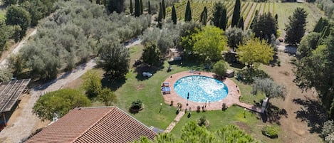 Una propiedad residencial con piscina rodeada de un jardín, techo de tejas y vistas al campo.