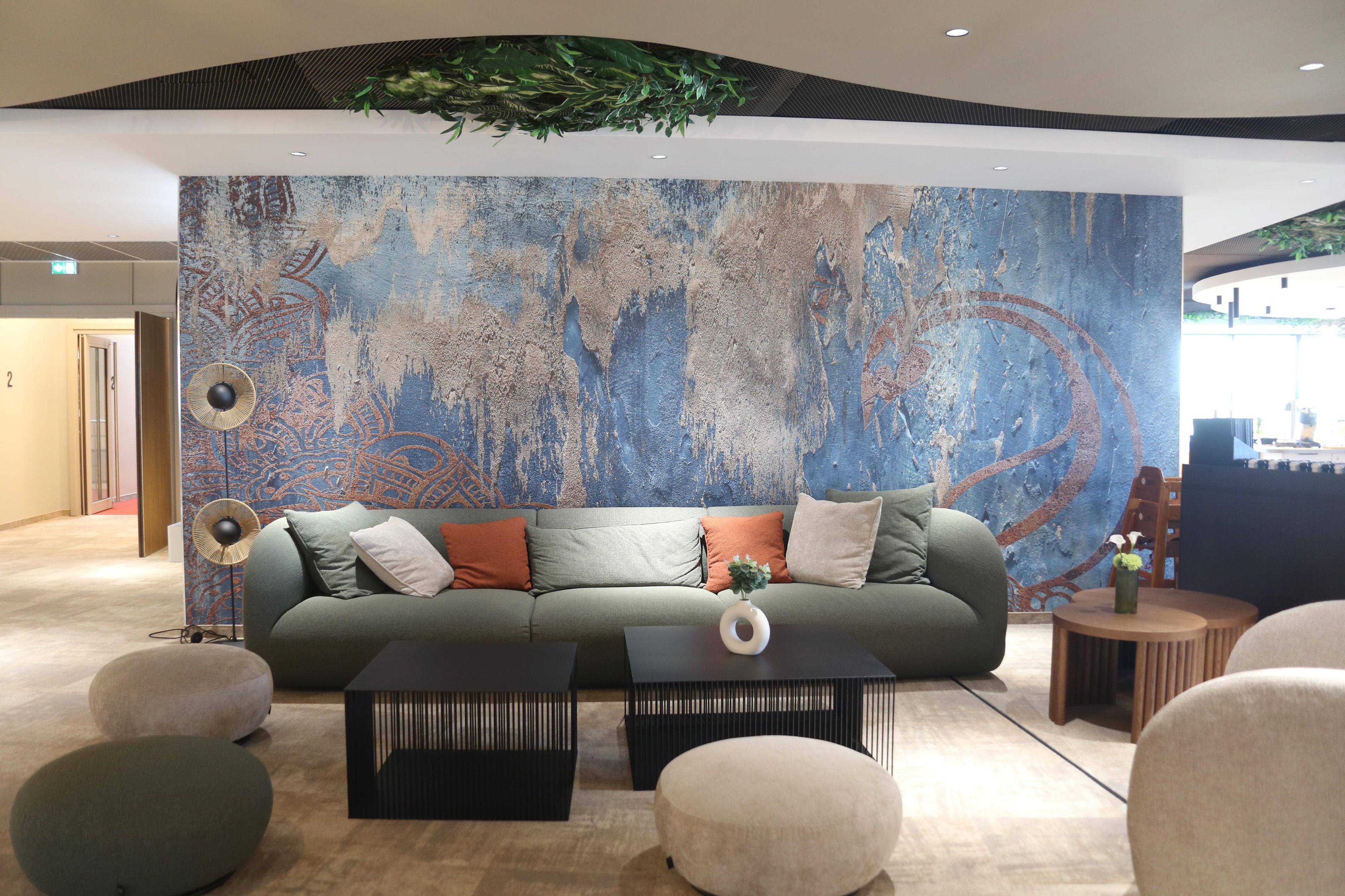 Un espace de détente moderne comprenant un canapé, une table basse et un pouf, agrémenté d’une grande fresque murale abstraite.
