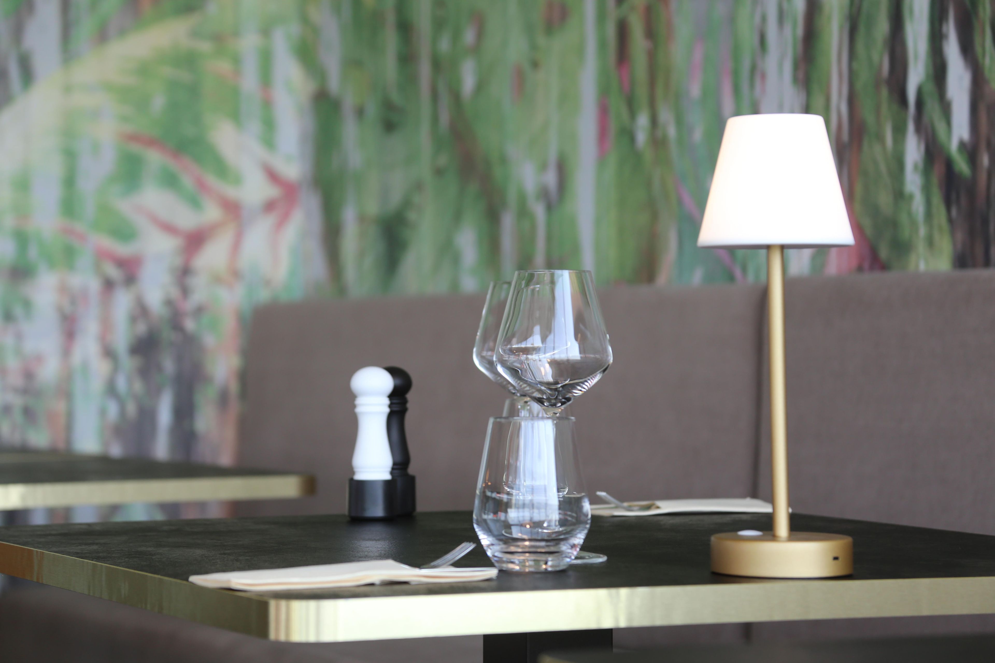 Une table à manger avec un plateau en verre transparent, un salier blanc et une lampe de table de couleur or.