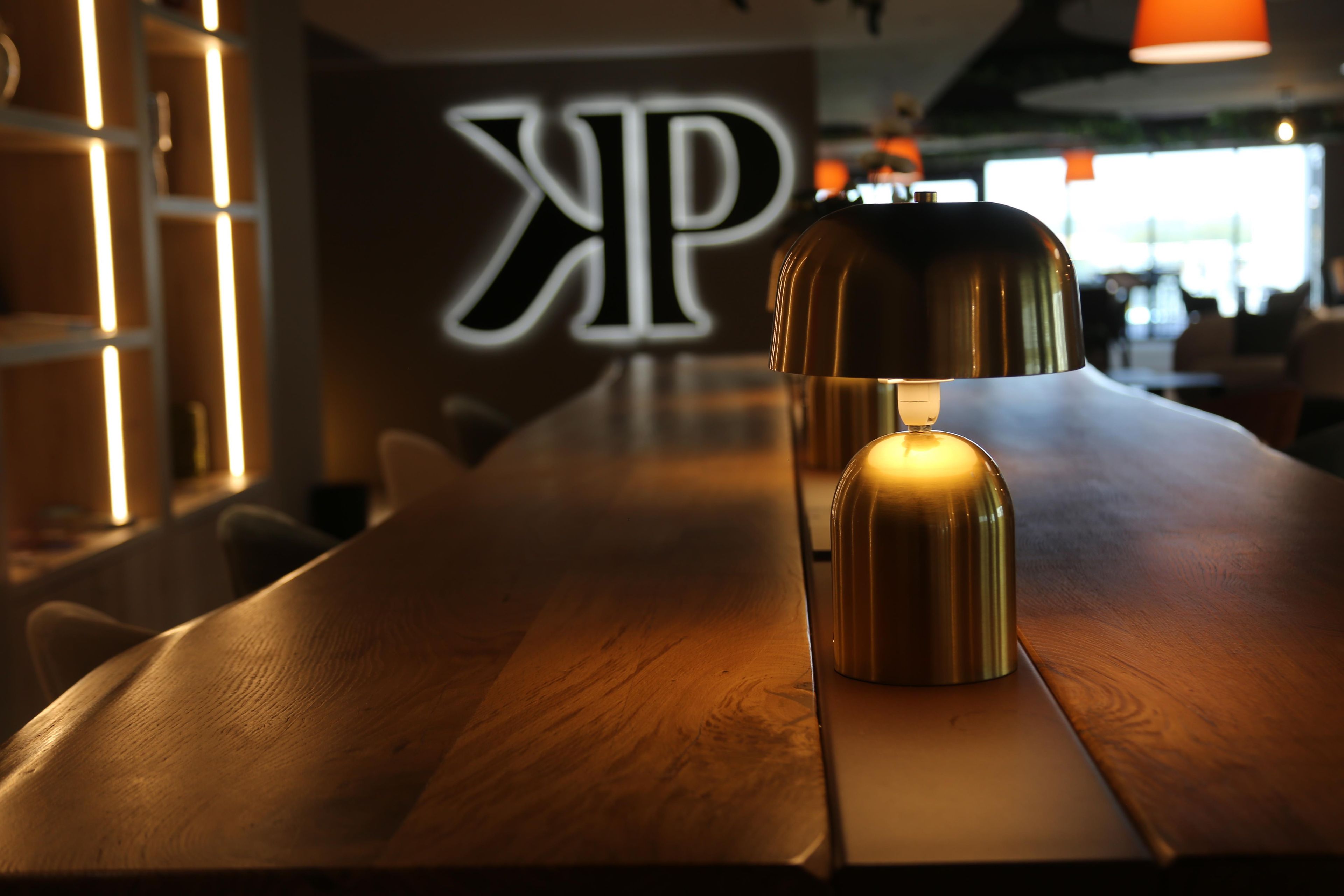 A table with a modern lamp and a logo in the background.