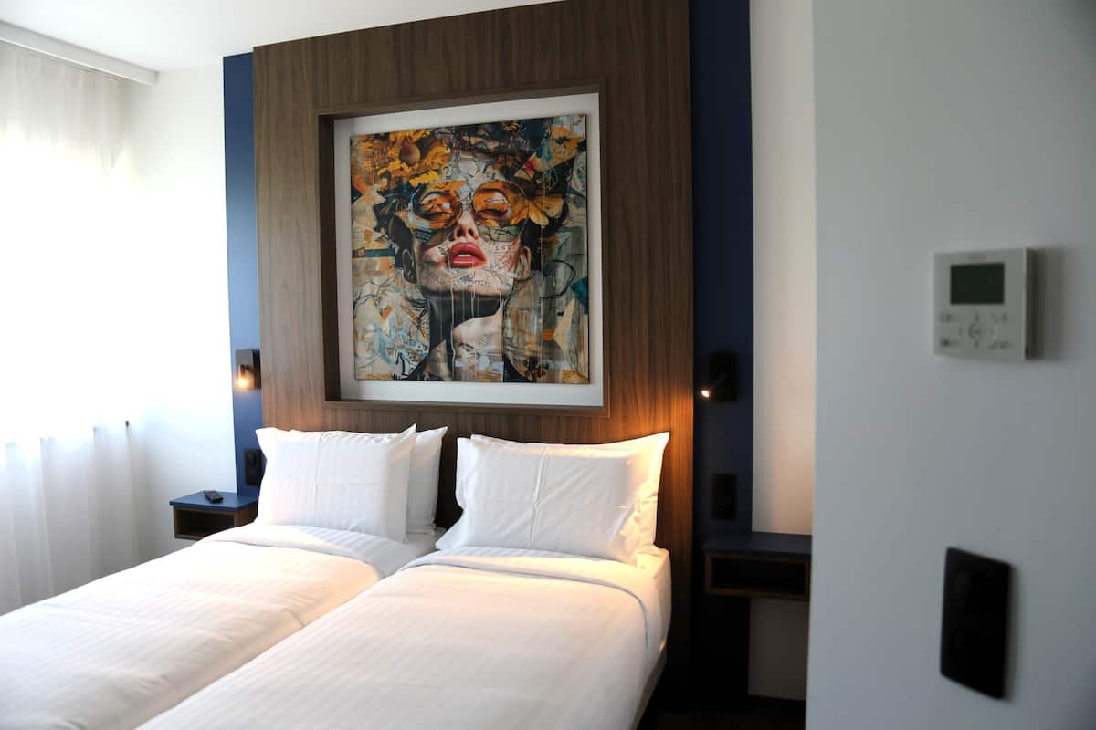 A hotel room with a large bed, two bedside tables, a wall-mounted artwork, and a thermostat.