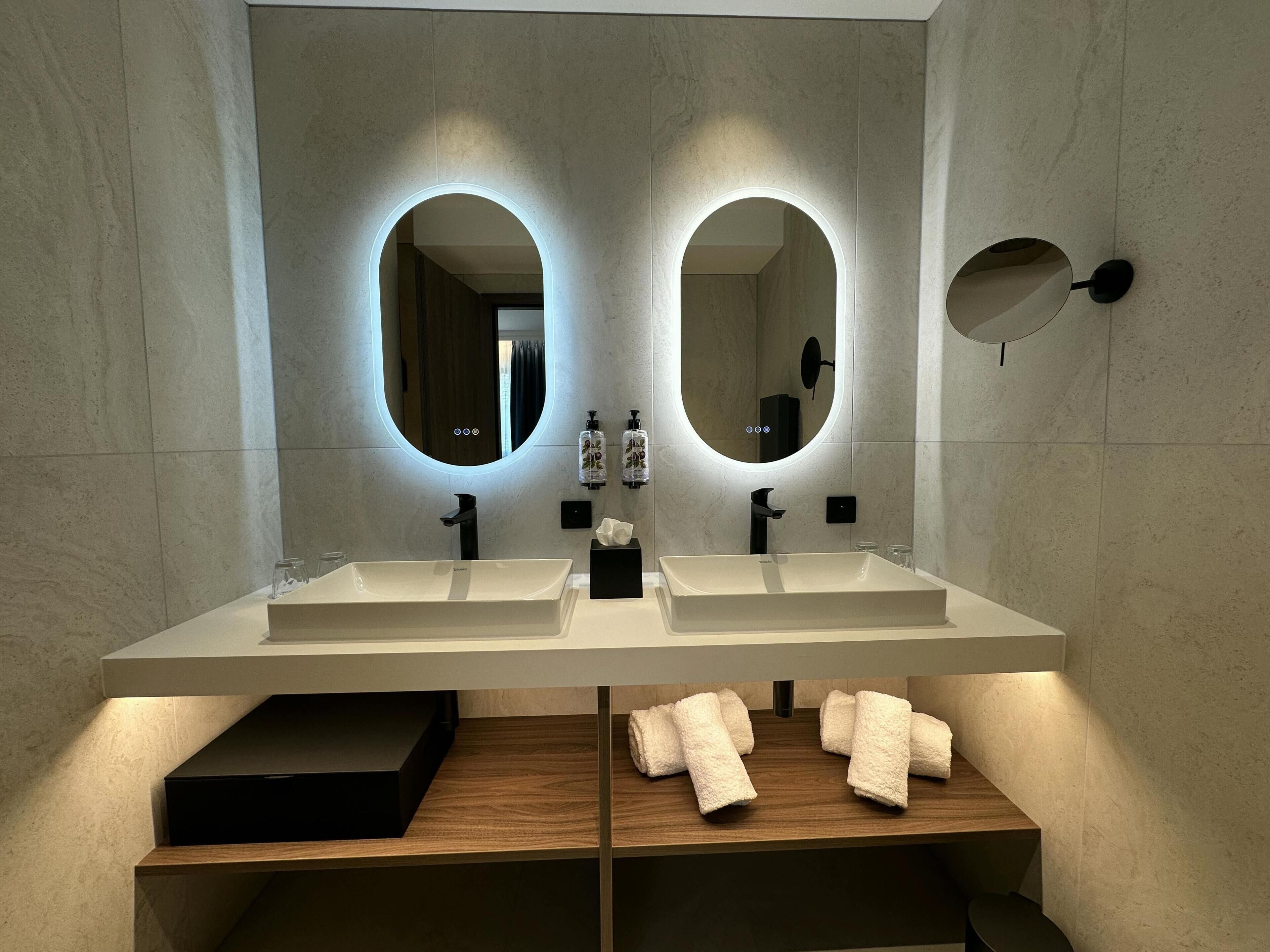 Un baño moderno con dos lavamanos, un espejo y un perchero para toallas.